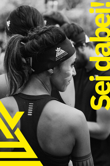 Zur Anmeldung Teilnehmerin von hinten abgebildet steht fokussiert am Start. Arlberger Wadlbeisser Logo als Designelement in gelb am linken Bildrand und Schriftzug "Sei dabei!" am rechten Bildrand. Bild in Graustufen.