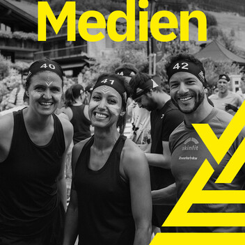 Zu den Bildern und Videos Drei Teilnehmer blicken glücklich und motiviert in die Kamera im Startbereich. Arlberger Wadlbeisser Logo als Designelement in gelb am rechten Bildrand und Schriftzug "Medien" am oberen Bildrand. Bild in Graustufen.